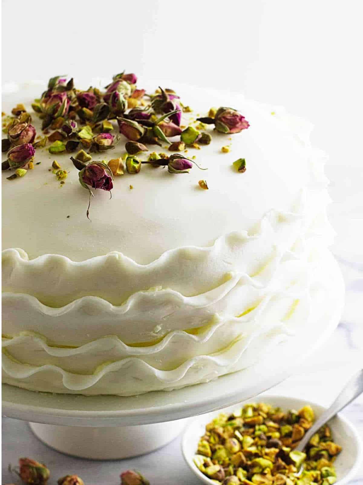adding rose buds and pistachio nuts on top of a cake.