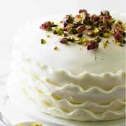 White layer cake on a cake pedestal with pistachios and rose buds on top.