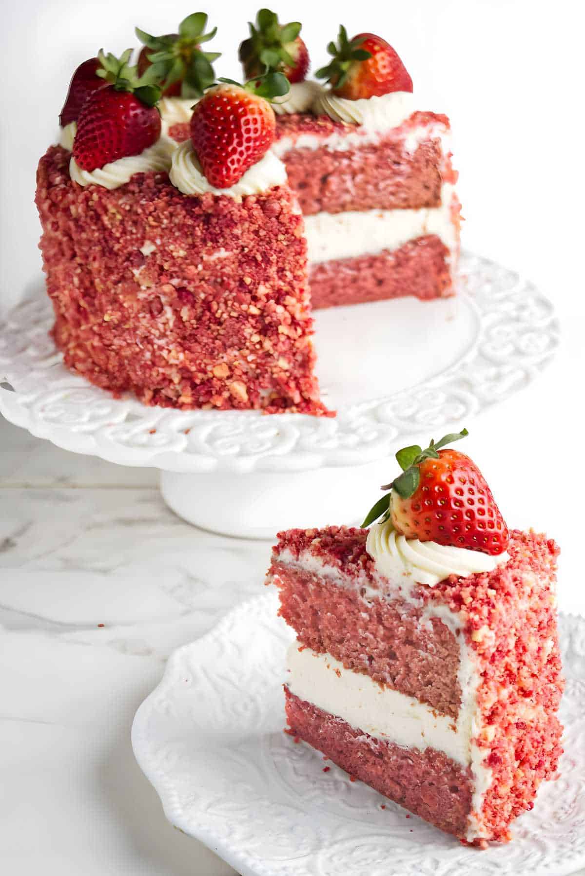 Strawberry crunch cake on a pedestal with a slice on a plate.