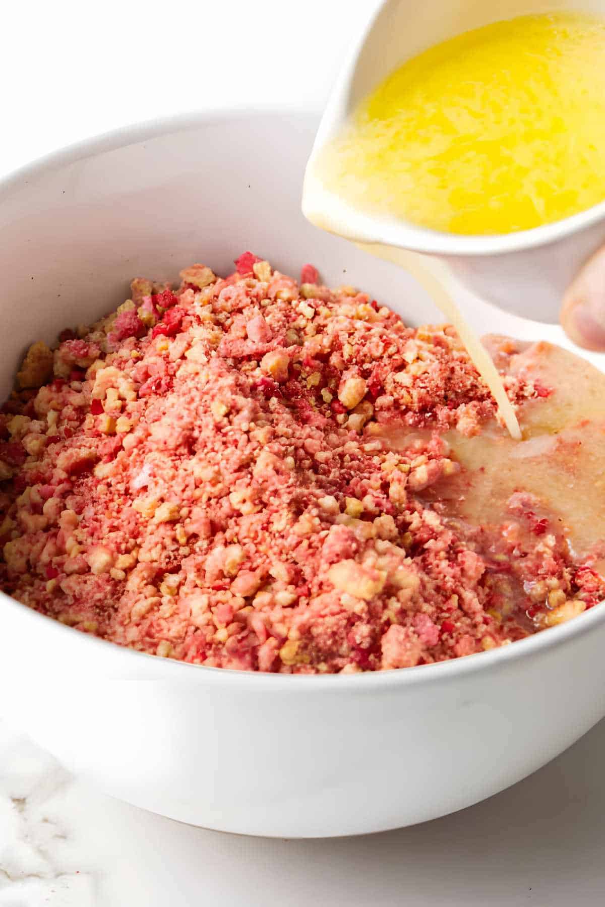 Adding melted butter to crushed pink crumbs.